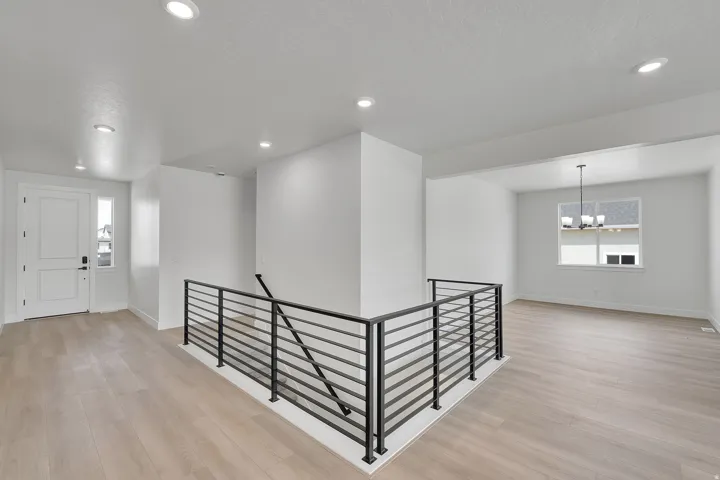 Recessed lighting illuminates the entryway, featuring wood-finish flooring and a contemporary black metal stair railing