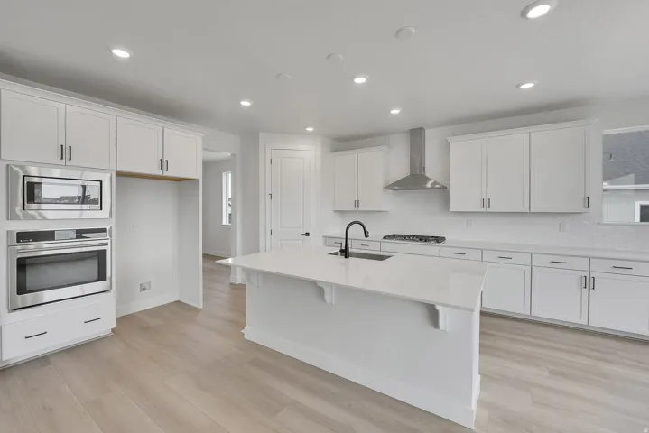 White cabinetry with sleek hardware, stainless steel appliances, a center island with sink, light wood-finish flooring, and recessed lighting