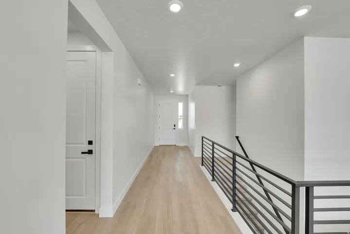 Light wood-finish flooring with recessed lighting, white walls, and a black metal railing