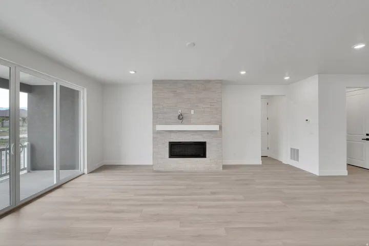 Recessed lighting, wood-finish flooring, and a fireplace with a light-toned stone surround and white mantel