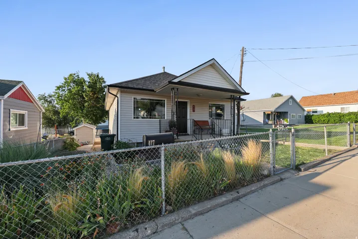 Siding exterior with a covered porch, dark roof shingles, and a chain-link fence