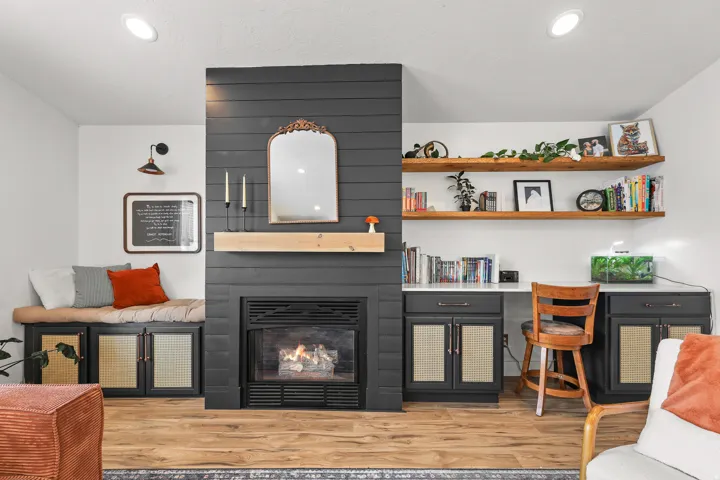 Fireplace with mantel, built-in bench seating with storage, integrated desk area, open wood shelving, and wood-finish flooring