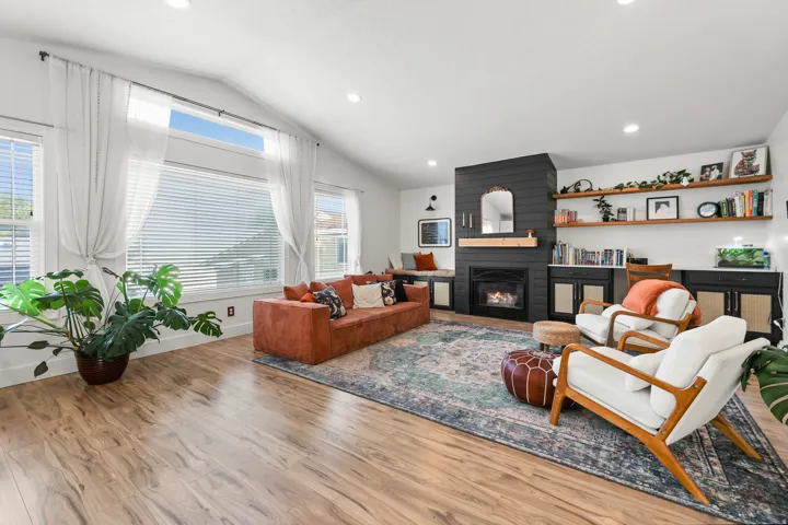 Vaulted ceilings, wood-finish flooring, a contemporary fireplace with a built-in hearth, and recessed lighting