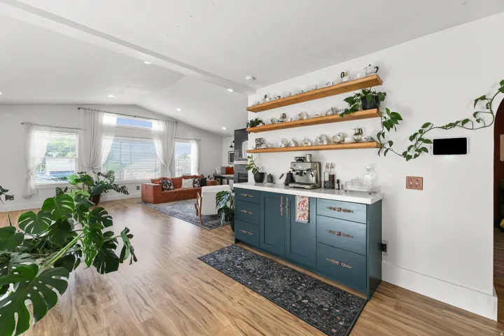 Wood-finish flooring, vaulted white ceilings, recessed lighting, expansive windows, and a built-in cabinet with open shelving