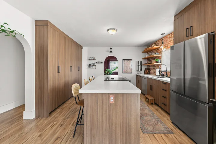 Kitchen with wood-finish flooring, an arched doorway, and an expansive island featuring a cooktop