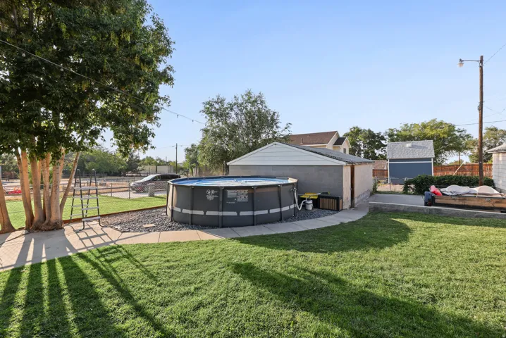 Expansive backyard featuring a manicured lawn, established trees, concrete pathways, and a detached garage with an additional storage shed