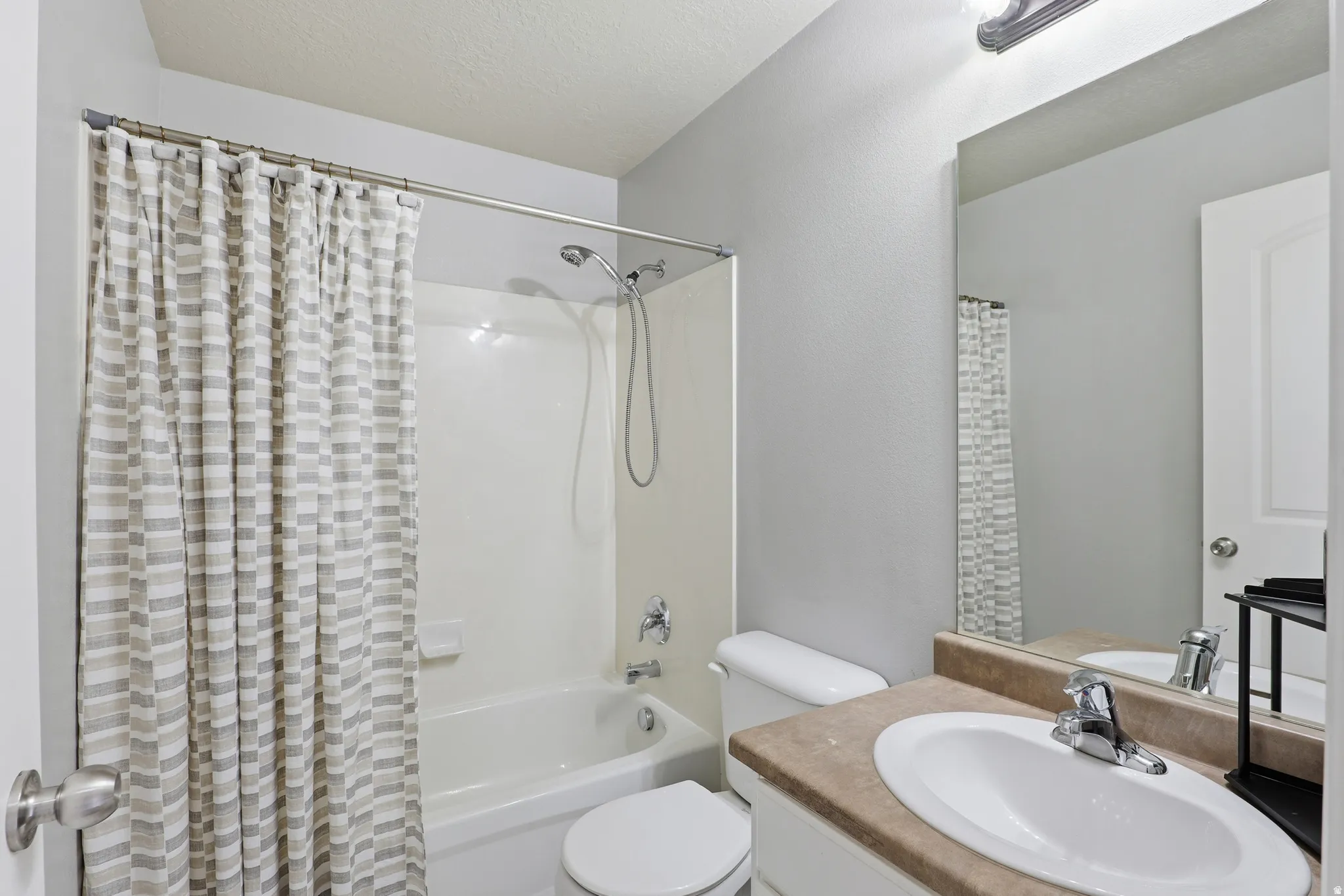 Bathroom featuring an integrated tub and shower with a curved shower rod, a single vanity with a laminate countertop, and an oval undermount sink