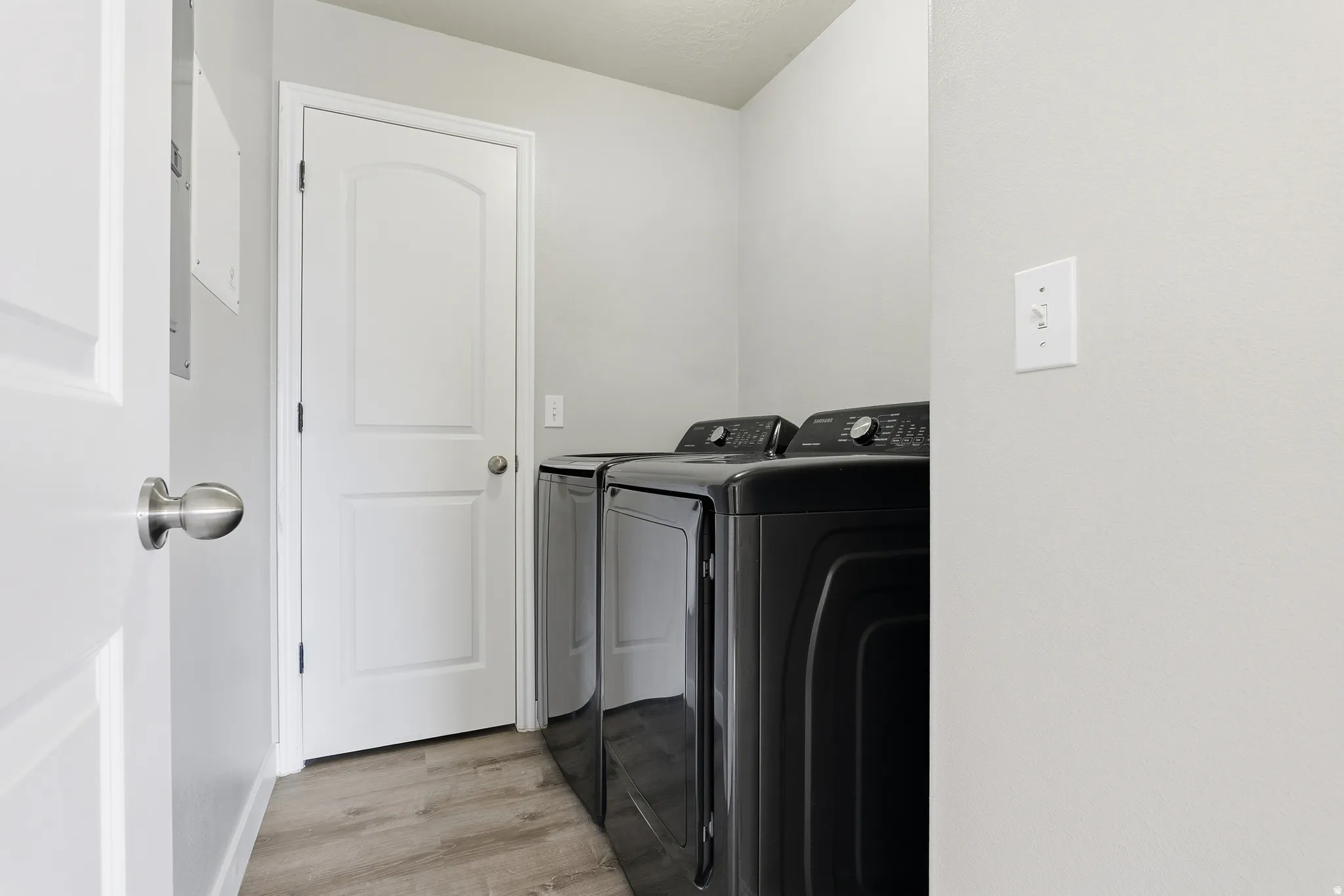 Laundry area featuring wood-finish flooring, light gray walls, and white doors with brushed nickel hardware