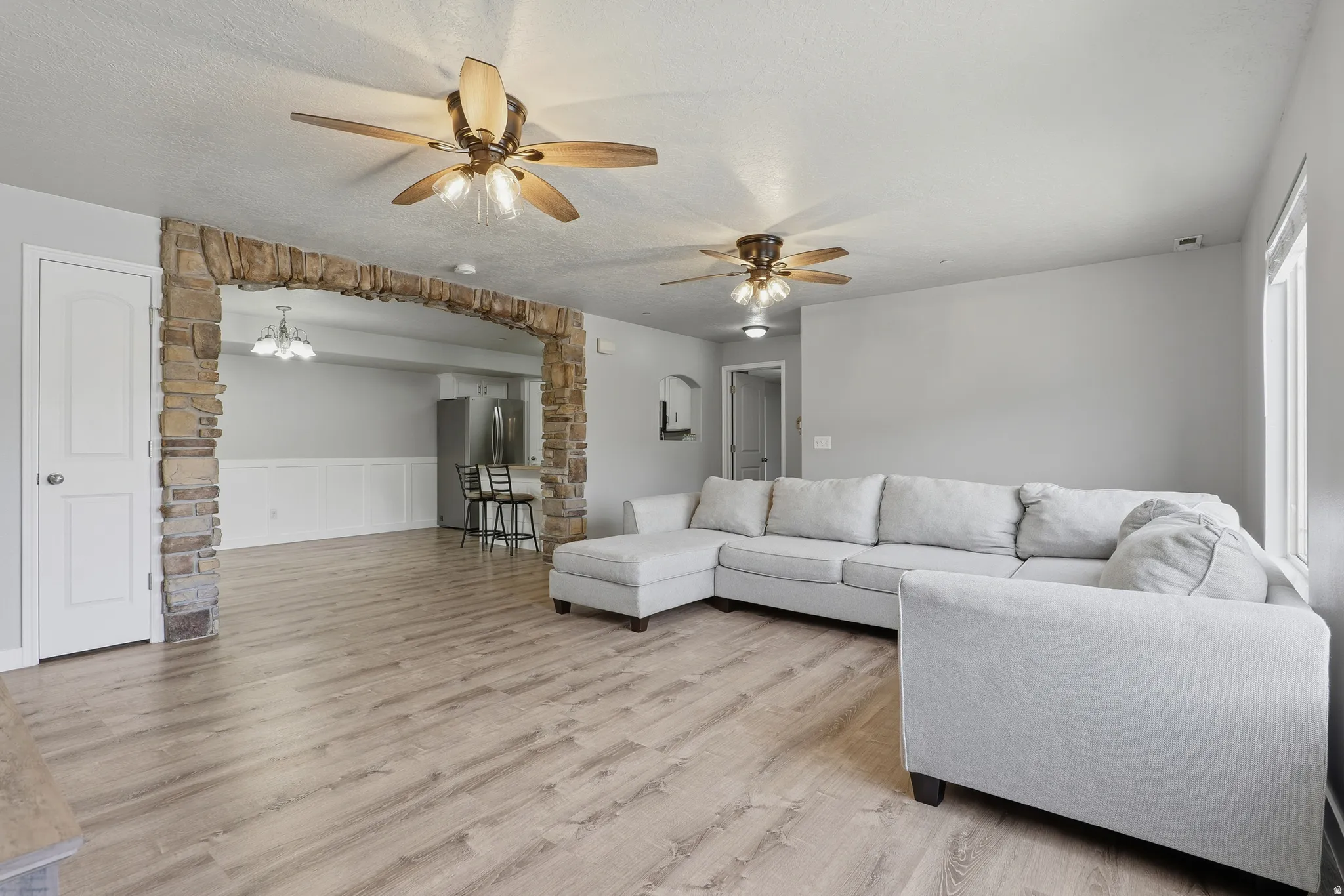 Stone archway entry, wood-finish flooring, ceiling fans with integrated lighting, white paneled door, large window with natural light