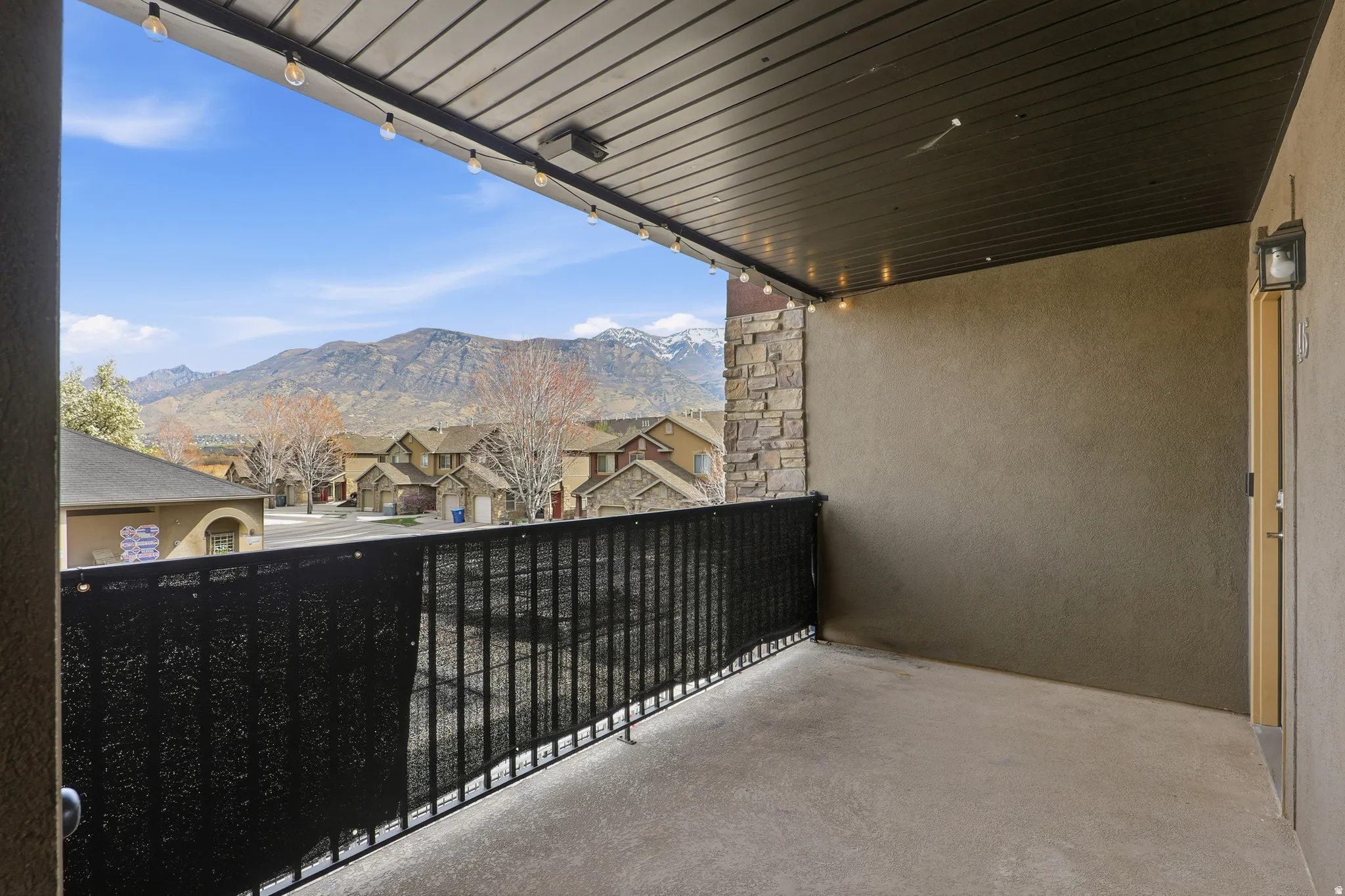 Outdoor balcony with concrete flooring, black metal railing, and a slatted ceiling