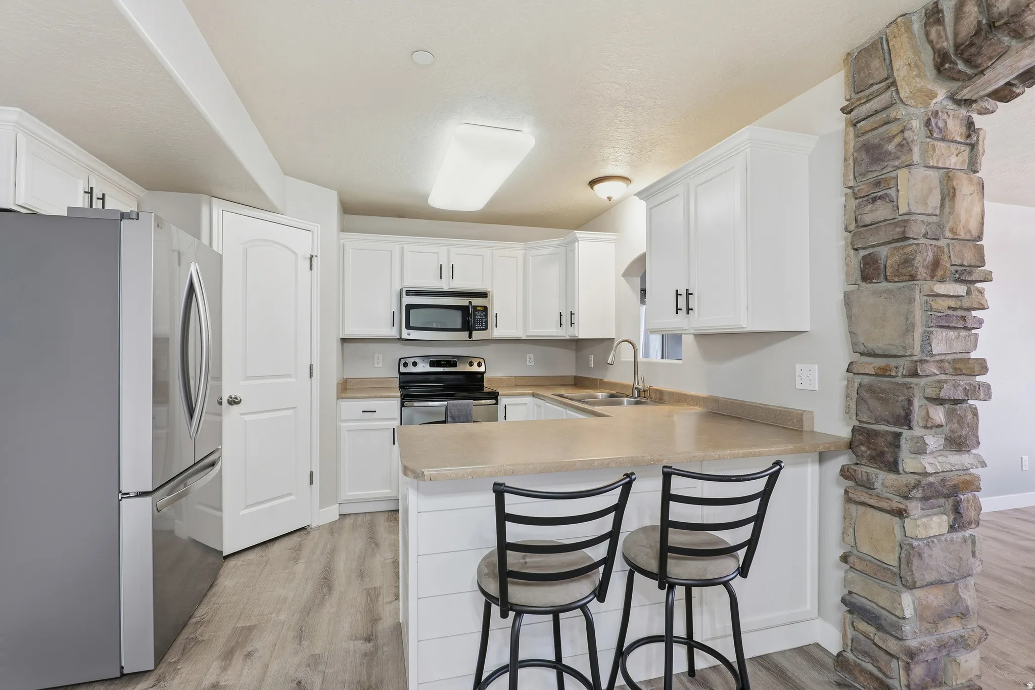 Kitchen with white cabinetry, stainless steel appliances, light-toned countertops, wood-finish flooring, and a stone archway feature