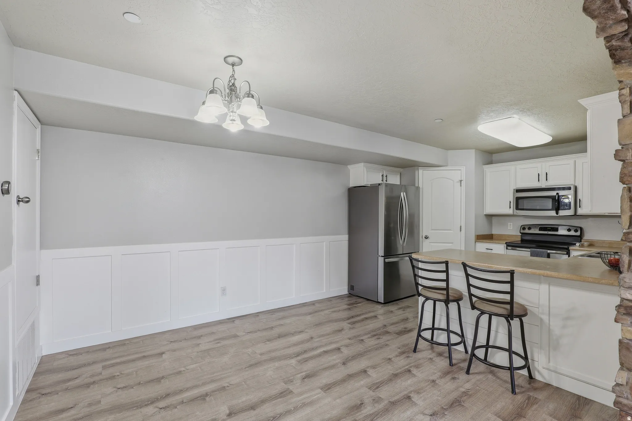 Wood-finish flooring throughout, white wainscoting, white cabinetry, stainless steel appliances, and a stone accent wall