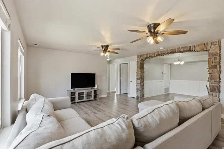 Expansive living area featuring wood-finish flooring, a stone archway, multiple ceiling fans with integrated lighting, and transom windows