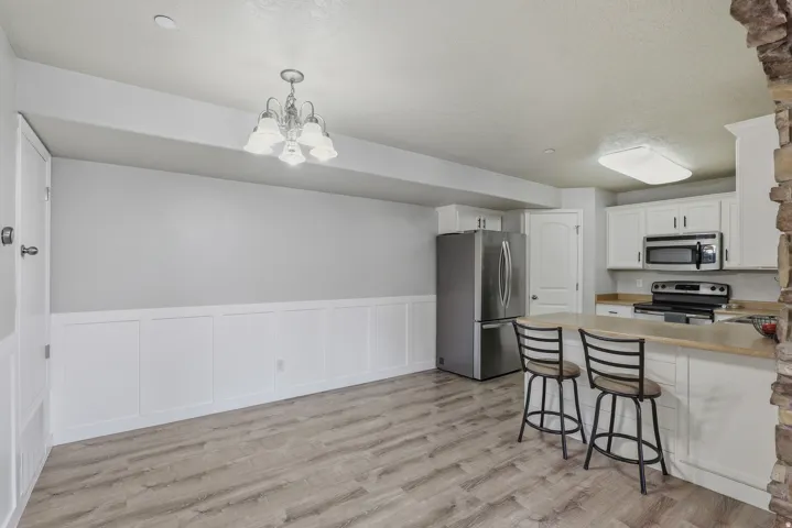 Wood-finish flooring throughout, white wainscoting, white cabinetry, stainless steel appliances, and a stone accent wall
