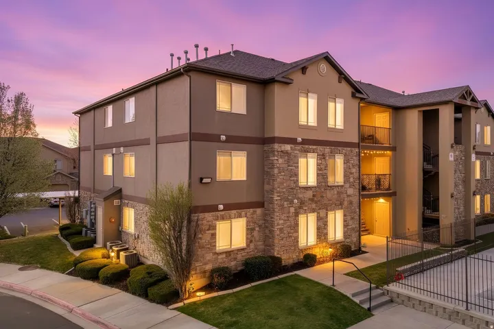 Multi-story building featuring stone and stucco exterior finishes, gabled rooflines, multiple windows, and a paved walkway
