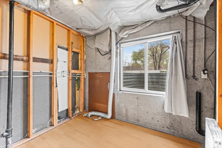 Basement space featuring exposed concrete walls, wood-finish flooring, and a single window