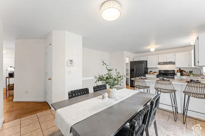 Open-concept dining area with tiled flooring, leading to a kitchen featuring white cabinetry, light-toned countertops, and black appliances