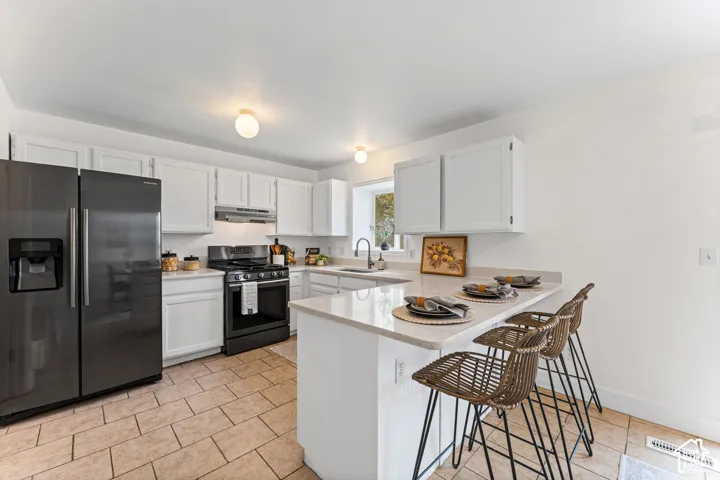 Kitchen featuring stainless steel appliances, white cabinetry, a light-colored countertop, an integrated breakfast bar, and tiled flooring