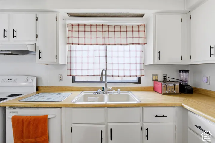 White cabinetry with black hardware, wood-finish countertops, stainless steel sink with gooseneck faucet, and white electric range