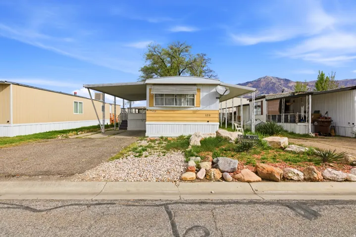 Exterior featuring a covered carport, gravel driveway, and a front yard with decorative rocks