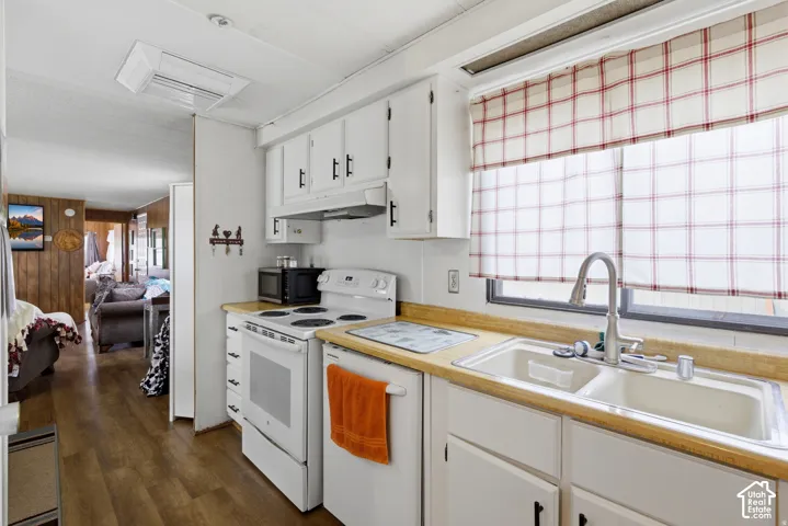 White cabinetry with matte black hardware, dual-basin sink with gooseneck faucet, white freestanding electric range, wood-finish flooring, and light-toned countertops