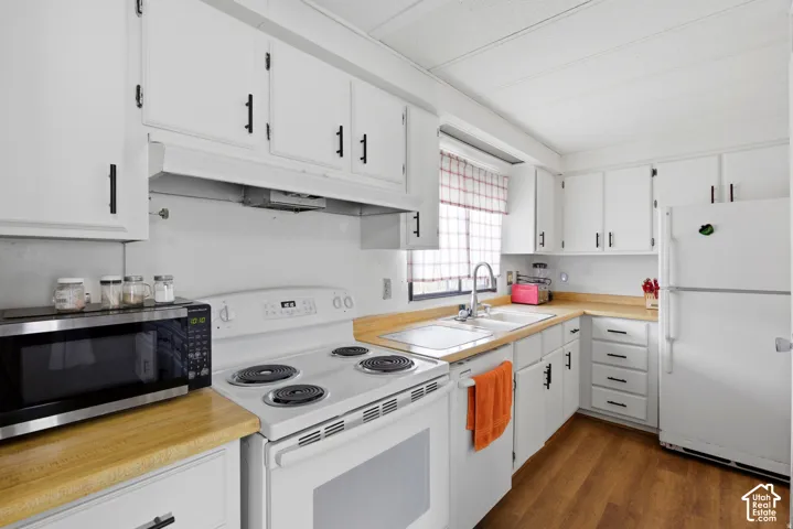 Bright kitchen featuring white cabinetry with black hardware, wood-finish countertops, and a white coil-top electric range