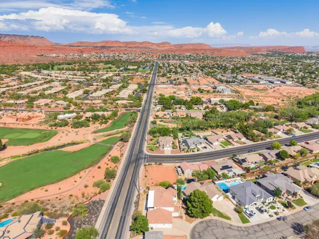 Expansive residential area with a prominent paved road, adjacent golf course, and distant red rock formations