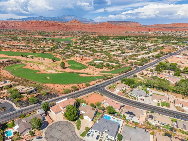 Expansive residential area with a prominent golf course, adjacent to a major roadway, with red rock formations in the background