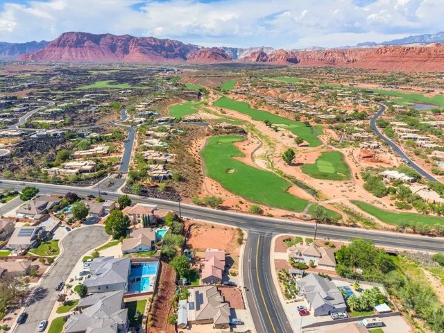 Expansive golf course with manicured greens, surrounded by residential properties and natural desert landscaping, set against a backdrop of red rock mountains