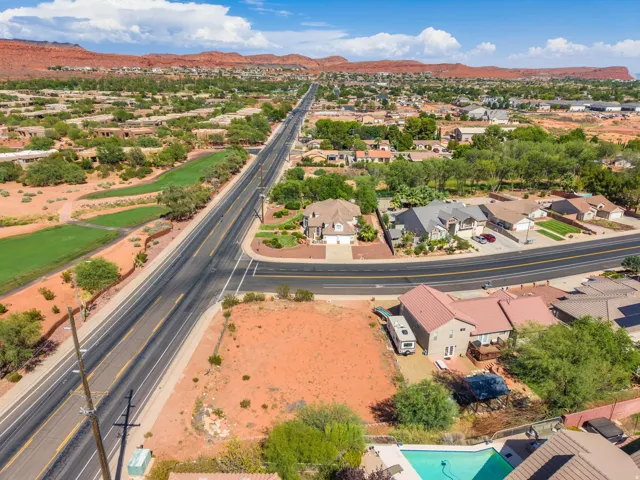 Expansive residential area with a long paved road, surrounded by residential structures, arid landscaping, and distant mountains