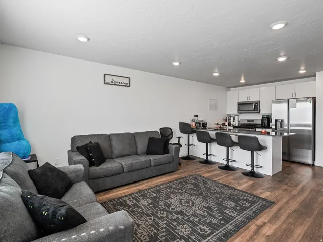 Recessed lighting throughout, wood-finish flooring, white cabinetry, stainless steel appliances, and a kitchen island with seating