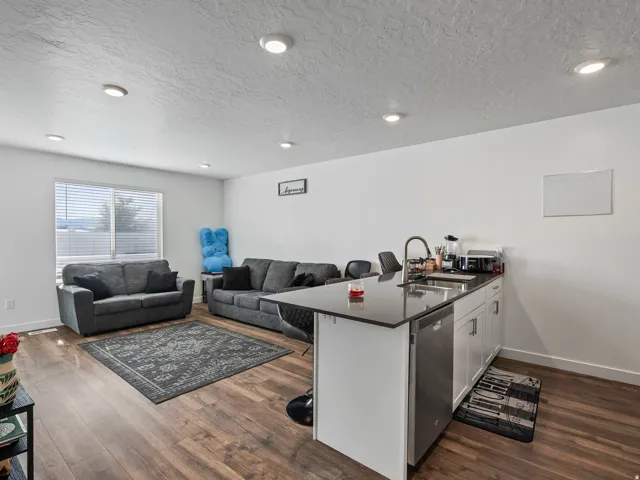 Open-concept living space with wood-finish flooring, recessed lighting, and a kitchen island featuring a sink and dishwasher