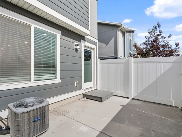 Concrete patio with white vinyl fencing, a glass-paneled exterior door, and an exterior wall light fixture