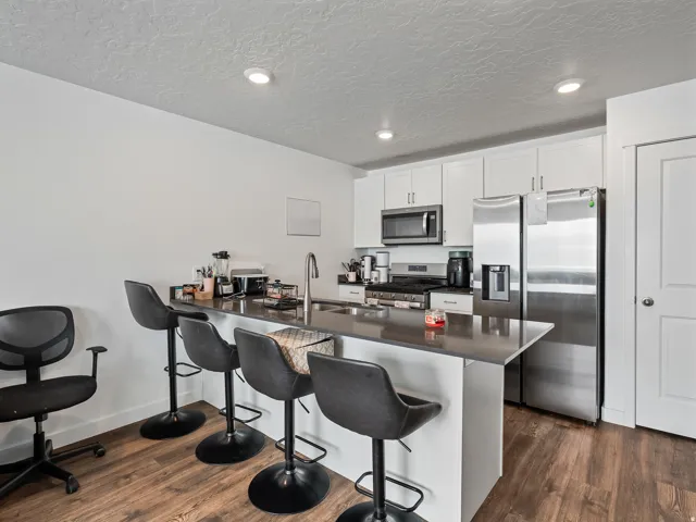 Kitchen featuring wood-finish flooring, stainless steel appliances, white cabinetry, a built-in microwave, and recessed lighting