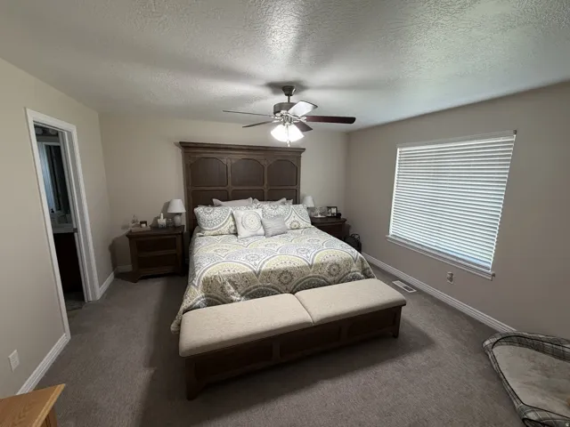 Carpeted bedroom featuring a ceiling fan with integrated lighting, a window with horizontal blinds, and a wood-finish headboard
