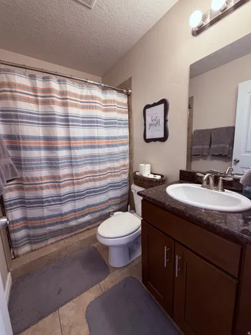 Vanity with a dark countertop and undermount sink, brushed nickel faucet, wood-finish cabinetry, and tile flooring
