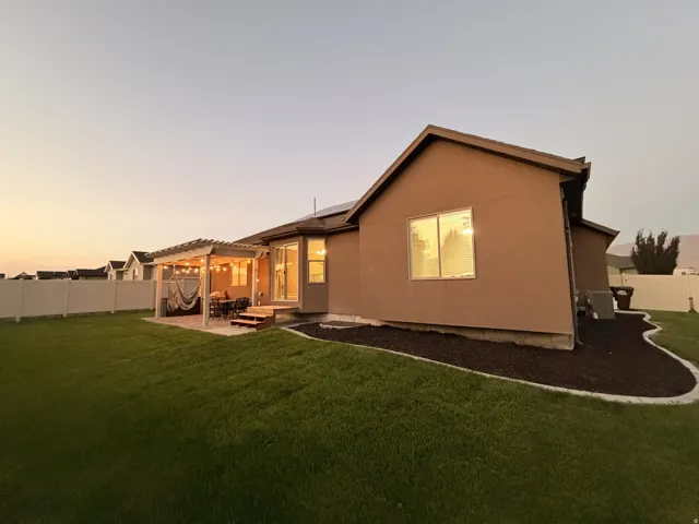 Expansive backyard featuring a pergola-covered patio, manicured lawn, and white privacy fencing