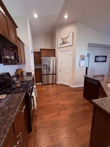 Kitchen featuring wood-finish flooring, dark wood cabinetry, stainless steel refrigerator, black range, and black built-in microwave