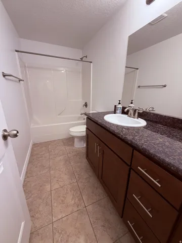 Spacious bathroom featuring a dark wood-finish vanity with a single basin sink, speckled countertop, and tiled flooring