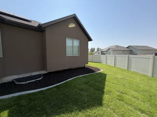 Expansive backyard featuring a manicured lawn, established landscaping beds with dark mulch, and a vinyl privacy fence