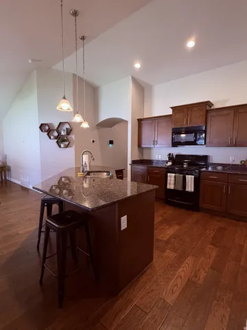 Kitchen island with stone-finish countertop, wood-finish flooring, recessed lighting, pendant lighting, and wood-finish cabinetry