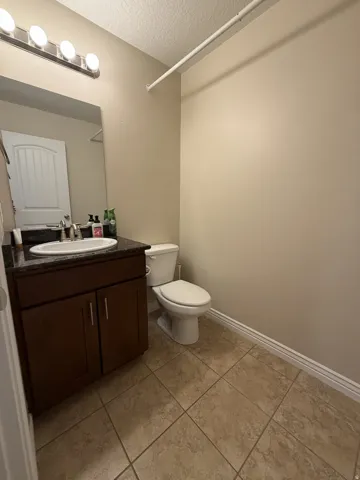 Bathroom featuring a dark wood-finish vanity with a dark countertop, an integrated sink, a wall-mounted mirror, and tile flooring