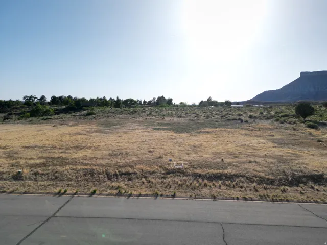 Expansive vacant land with a paved road frontage, backed by distant mountains and natural vegetation
