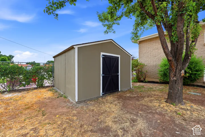Detached storage shed with a solid roof, featuring a chain-link fence boundary and mature trees