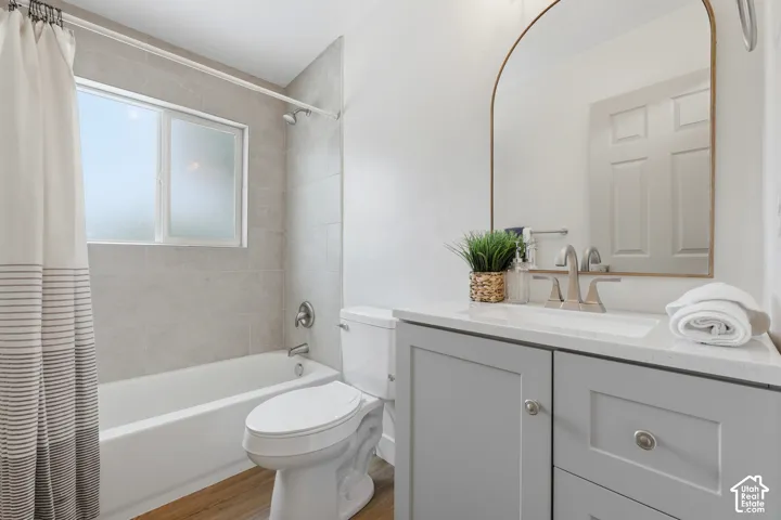 Bathtub with subway tile surround, wood-finish flooring, light gray vanity with white countertop, and an arched mirror