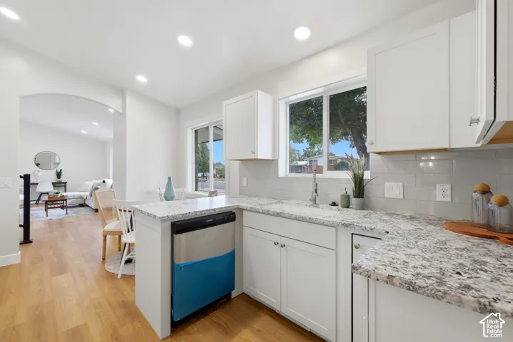 Kitchen featuring white cabinetry, light-toned countertops, a stainless steel dishwasher, a single-basin sink, and wood-finish flooring