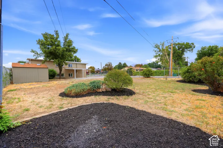 Spacious exterior featuring a detached storage shed, covered patio, mature trees, and landscaped garden beds