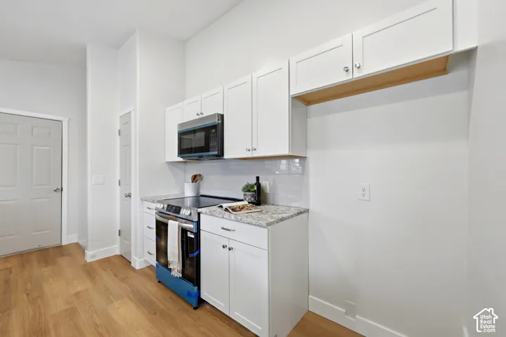 Kitchen featuring white shaker-style cabinetry, stainless steel microwave, electric range, light-toned countertops, and wood-finish flooring