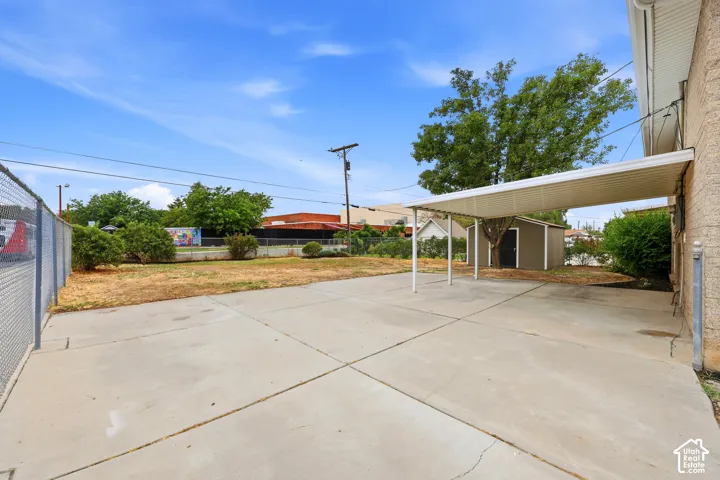 Expansive concrete driveway with a covered carport, chain-link fencing, and a detached storage shed