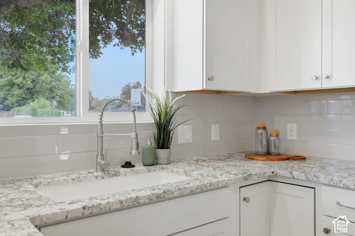White shaker cabinetry, light-toned granite countertops, a large single-basin sink, and a stainless steel pull-down faucet